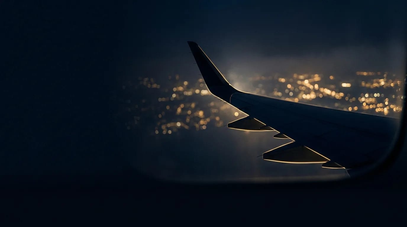 Asa de avião vista pela janela, sobre as luzes de uma cidade à noite