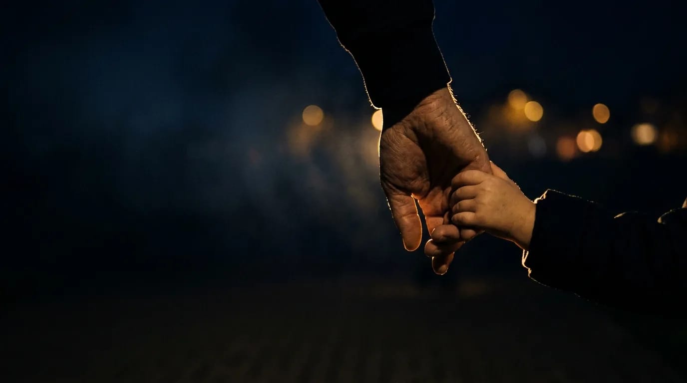 Mão de um adulto segurando a mão de uma criança, contra uma luz dourada